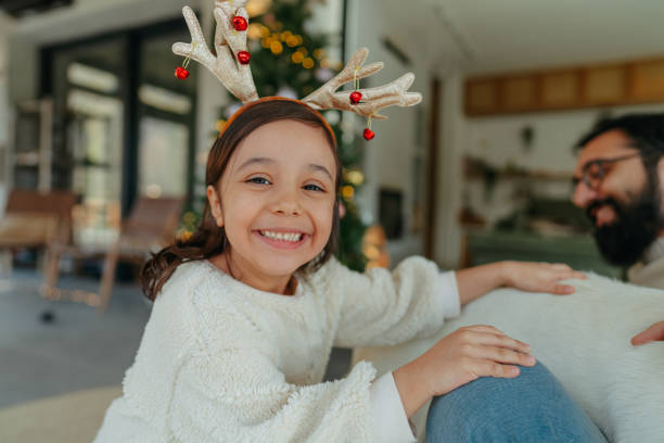 Photo of a little smiling girl with reindeer antlers celebrating Christmas in her home
