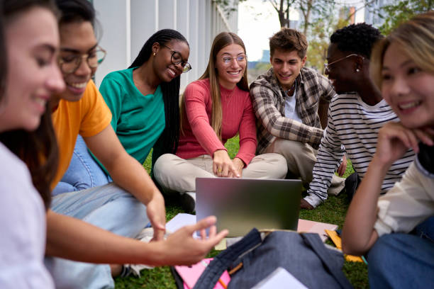istock Group diverse Gen z university joyful students going through syllabus sitting on lawn in campus park 2173438420