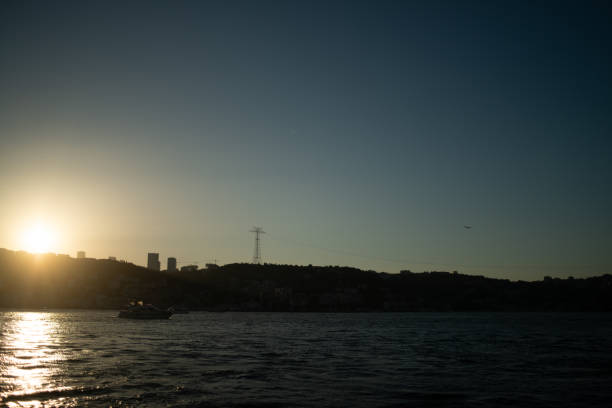 A breathtaking view of the Istanbul Bosphorus at sunset, featuring the iconic Turkish flag waving proudly. The golden light reflects on the water, highlighting the city's historic skyline and creating a serene, picturesque scene.