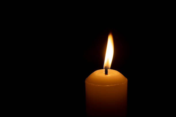istock A single burning candle flame or light glowing on a big white candle isolated on black or dark background on table in church for Christmas, funeral or memorial service 2173446845