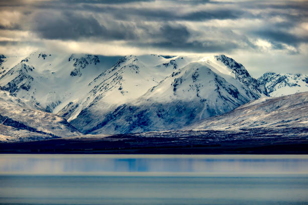 A moody cloudscape over the calm water on a;lpimne Lake Tekapo