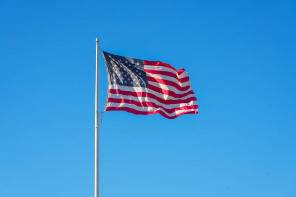 istock waving USA flag on pole against blue sky 2173468786