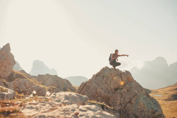 Young woman sits on boulder in mountain meadow