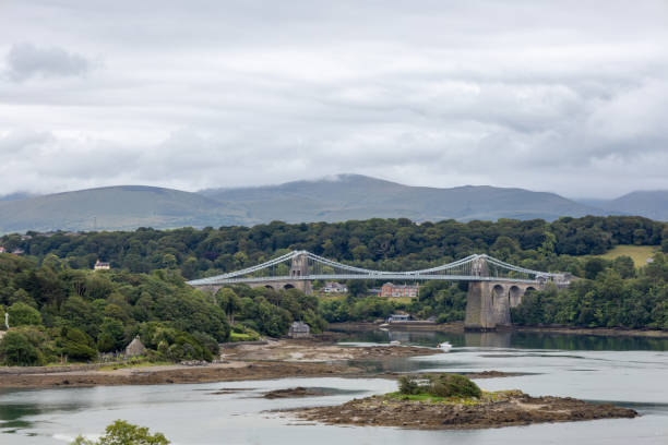 Anglesey, Wales - July 30, 2024: This image shows a landscape view of the Menai Suspension Bridge (Pont y Borth), crossing the Menai Strait between the island of Anglesey and mainland Wales.