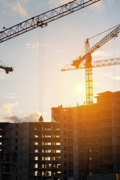 istock Cranes operate at a construction site during sunset, with workers actively engaged in building activities on the structure 2173478419