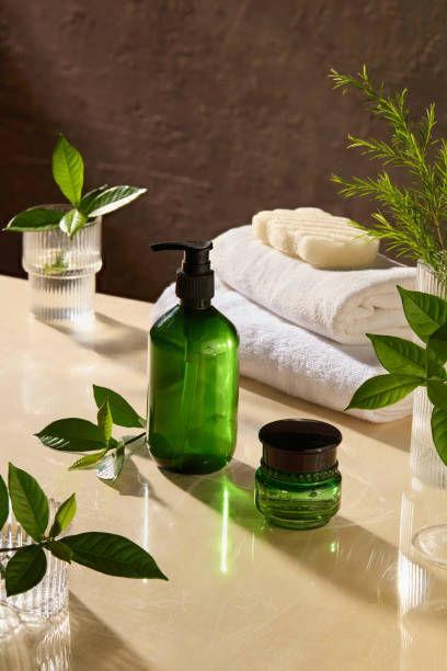 istock Natural spa theme photo with unlabeled green pump bottle and moisturizer pot placed by side on light yellow spa table top, next to some glass jars contain green plant, bath towel and soap 2173478654