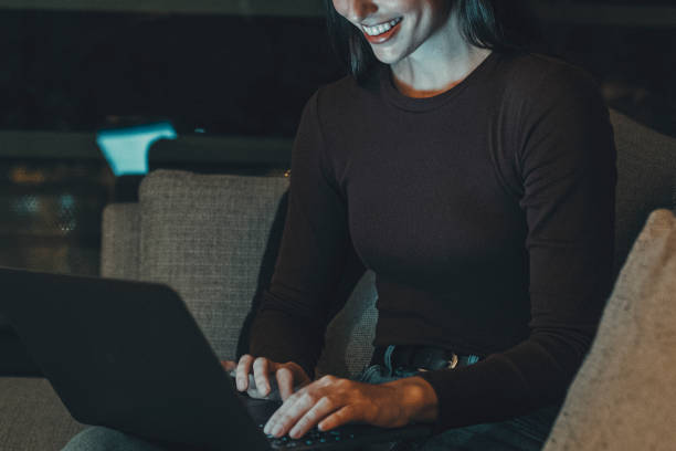 istock Young woman sitting on a hotel room sofa in the evening, using a laptop for remote work or chatting with friends and family. Embracing the modern digital nomad lifestyle and nighttime productivity 2173488497