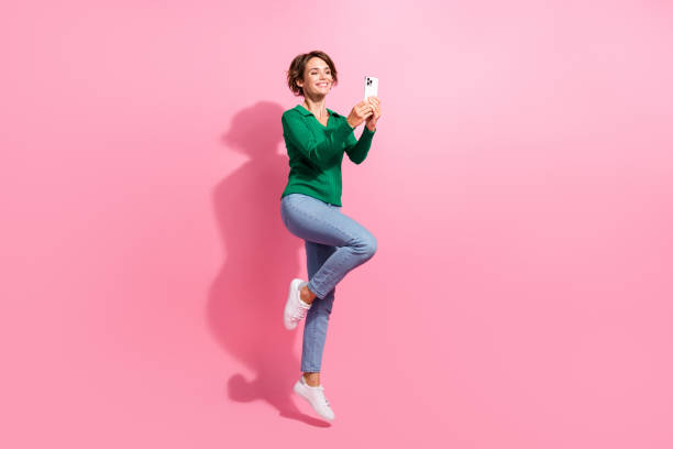 istock Full body photo of cheerful jumping girl using apple iphone new face id function high productivity device isolated on pink color background 2173490934