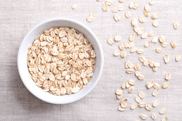 Rolled oat flakes, rolled oats in a white bowl on linen. Husked and steamed oat groats rolled into flakes and lightly toasted. Whole-grain food from husked common oats, Avena sativa, a cereal grain.