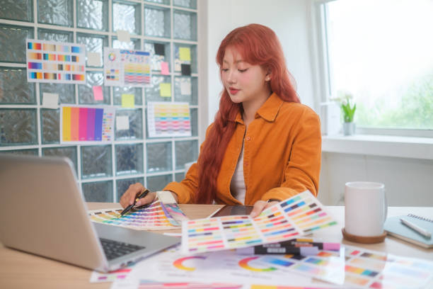 istock Young graphic designer with red hair is focused on her work, selecting colors for her project at desk. 2173535198