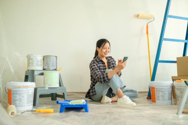 istock Smiling young woman using mobile phone, taking a break from painting during a home renovation project. 2173535931