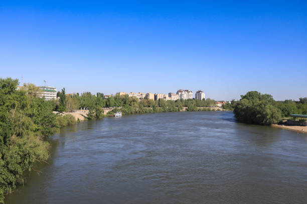 The river flows calmly through Tiraspol, surrounded by greenery and buildings under a bright blue sky, showcasing a serene urban landscape.