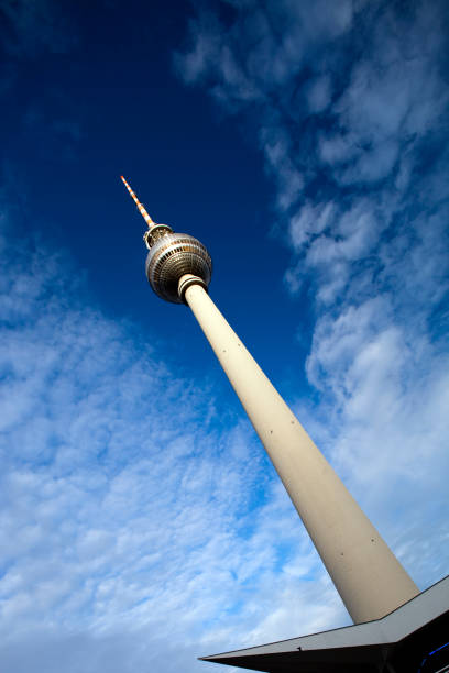 The iconic Fernsehturm rises above the city, showcasing Berlins skyline under a clear, blue sky filled with clouds.