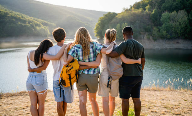View of young multiracial friends embracing while standing in front of a lake