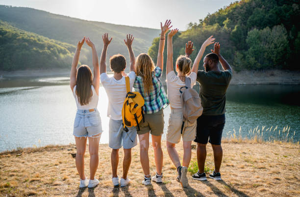 View of young multiracial friends with outstretched arms while standing in front of a lake