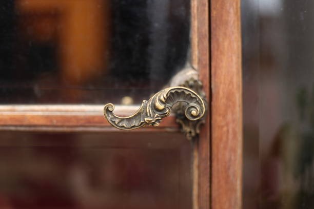 Mid shot of antique brass door-handle with scroll curvilinear scalloped decoration with a small bow, a timber framed glass panelled door the background.