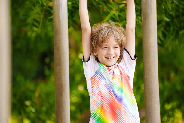 A young boy wearing a warm hat and jacket happily playing on an outdoor climbing wall on a sunny day. Childhood recreation and active lifestyle. A child aged 4 years (four years old)