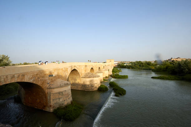 istock shows a historic stone bridge with large, rounded arches spanning a calm river 2173580128