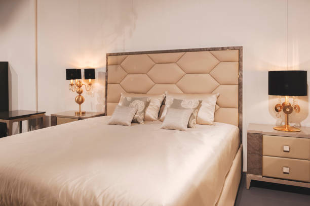 istock A bed with a white headboard and pillows, and a nightstand with a lamp. The room has a luxurious and elegant feel, with the bed and nightstand being the main focal points 2173603621