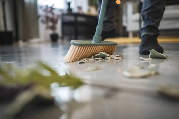 istock Adult man sweep broken vase pieces from a white, shiny floor surface 2173605307