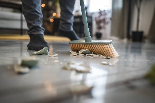 Adult man sweep broken vase pieces from a white, shiny floor surface