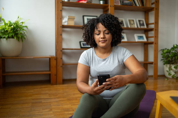 istock Young woman using smartphone while sitting on yoga mat at home 2173624472