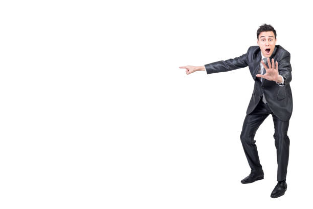 Full body of amazed male in formal suit pointing aside with outstretched arm and looking at camera with opened mouth isolated on white background