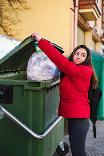 istock Pretty spanish woman with red coat throwing garbage into trash bin. 2173638662
