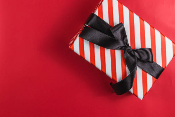 istock Red gift box with white stripes and a black bow on a red background 2173663427