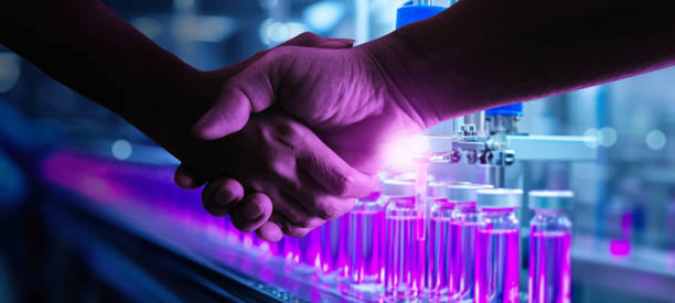istock Two individuals shake hands in front of advanced laboratory equipment, symbolizing a partnership or agreement in the pharmaceutical industry. 2173667078