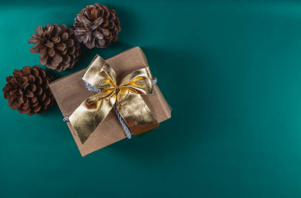 Christmas gift box with golden bow, pine cones on green background