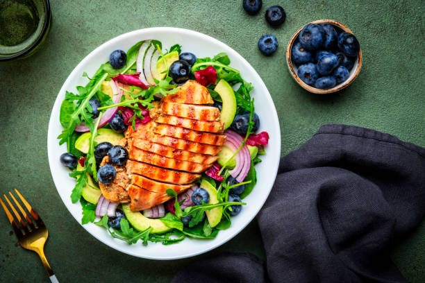istock Green salad with grilled chicken, avocado and blueberries, rustic background, top view 2173689641