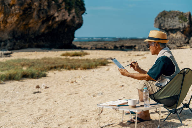 Senior man painting the coastline using watercolor while sitting on a beach