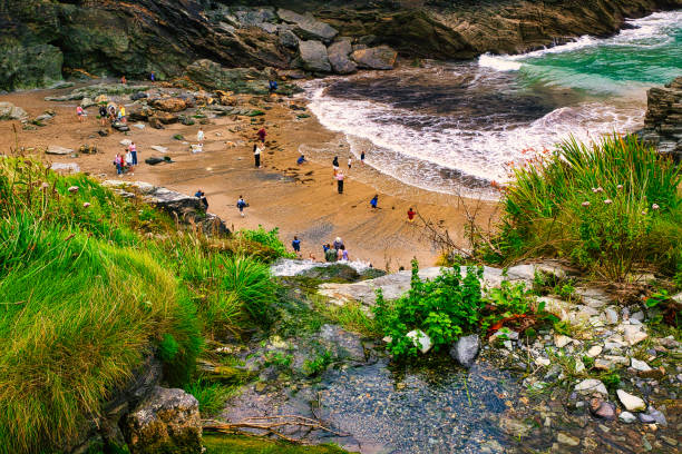 A scenic beach view with people enjoying the sandy shore, surrounded by rocky cliffs and lush greenery. The turquoise waves gently lap at the beach, creating a tranquil atmosphere.