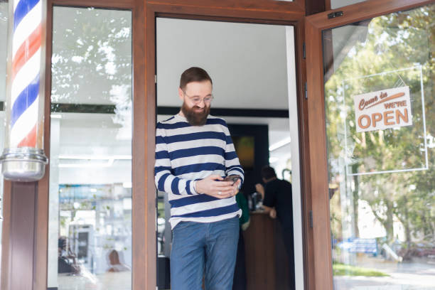 istock Bearded man standing outside barbershop checking phone 2173714004