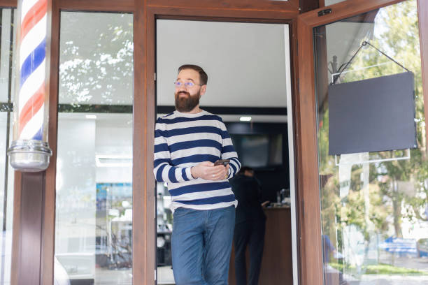Bearded man standing outside barbershop with  sign