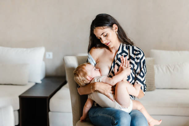 Happy young mother breastfeeding her baby boy at home stock photo
