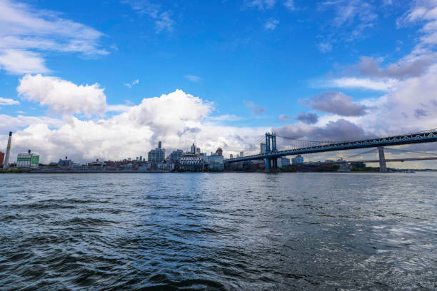 New York. USA. 09.22.2024. Waterfront view of Brooklyn Bridge and New York skyline under cloudy sky.