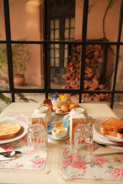 istock Pretty breakfast table setting in dining area by tall windows, in front of garden courtyard with firewood. Rustic cozy mood in hotel, hostel stay or guesthouse in Colonia del Sacramento, Uruguay 2173725710