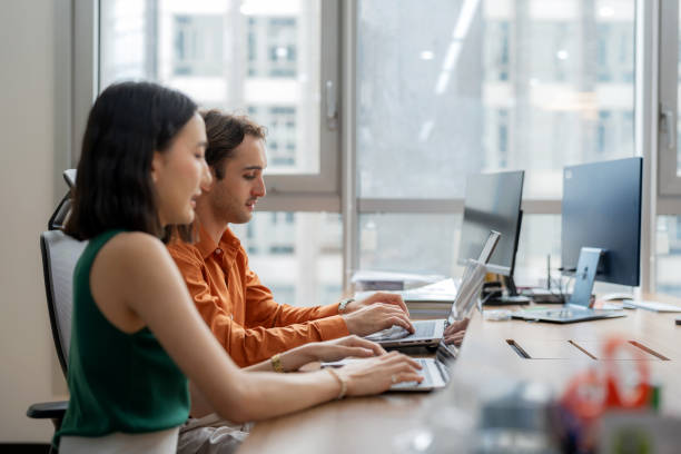 A team of digital marketers engages in a strategy discussing, using laptops to discuss and analyze various marketing channels for new products and services in a modern business setting. Both professionals collaborates on data-driven decisions and customer