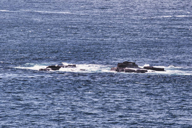 A rocky outcrop surrounded by ocean waves, showcasing the natural beauty of coastal landscapes. The water is a deep blue, with white foam from the waves crashing against the rocks.