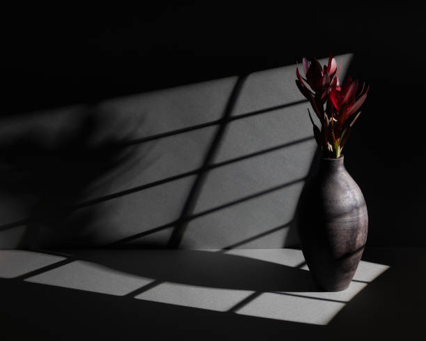 A beautifully crafted ceramic vase holds striking red flowers, illuminated by dramatic shadow patterns from a window. The minimalist composition evokes a sense of elegance and tranquility.