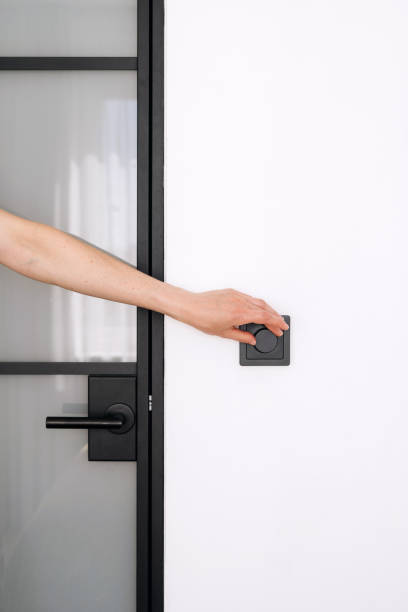 istock A hand reaching to turn on a light switch next to a modern glass door 2173743262