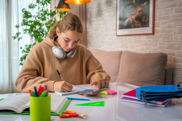 istock Schoolgirl doing school assignment at home. She is writing and using mobile phone 2173752835