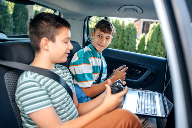 istock Teenagers on back seat of car using wireless technology before going to school and playing video games using game controller 2173801048