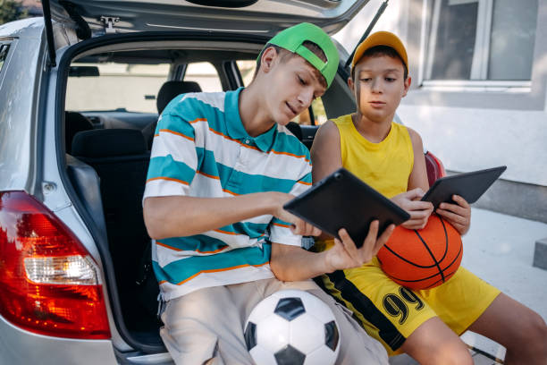istock Teenagers sitting in car trunk using digital tablet before leaving on sport training 2173801204