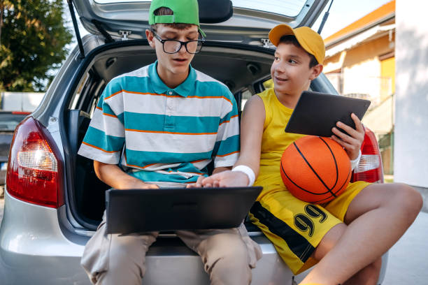 istock Teenagers sitting in car trunk using digital tablet before leaving on sport training 2173801210