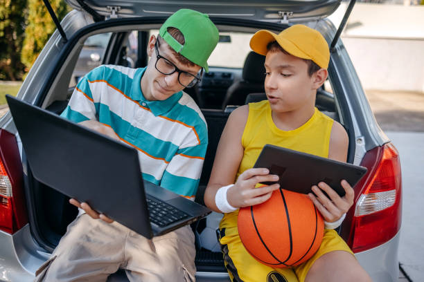 istock Teenagers sitting in car trunk using digital tablet before leaving on sport training 2173801215