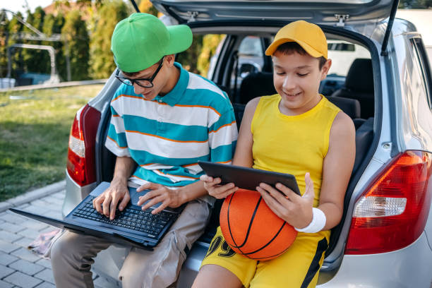 istock Teenagers sitting in car trunk using digital tablet before leaving on sport training 2173801216