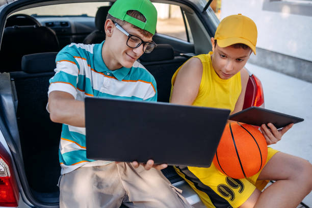 istock Teenagers sitting in car trunk using digital tablet before leaving on sport training 2173801237